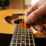 Main tenant un médiator sur les cordes d'une guitare acoustique